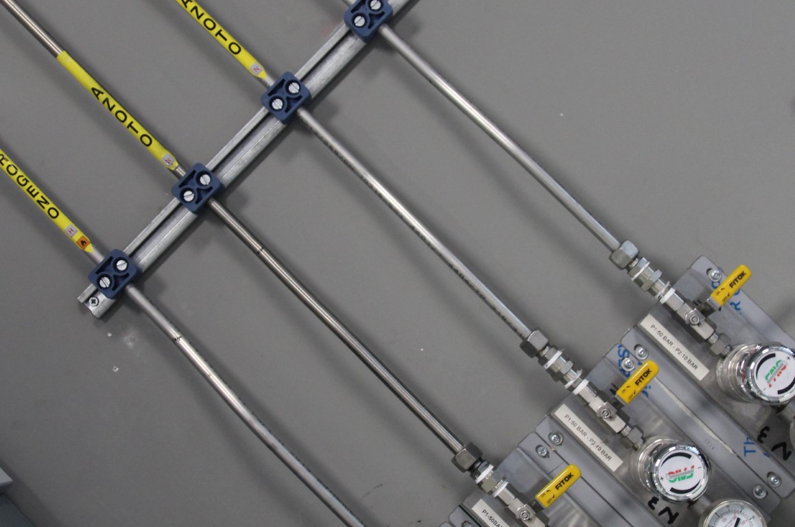 Dettaglio tecnico di tubazioni e manometri industriali in acciaio con valvole gialle e indicatori di pressione.