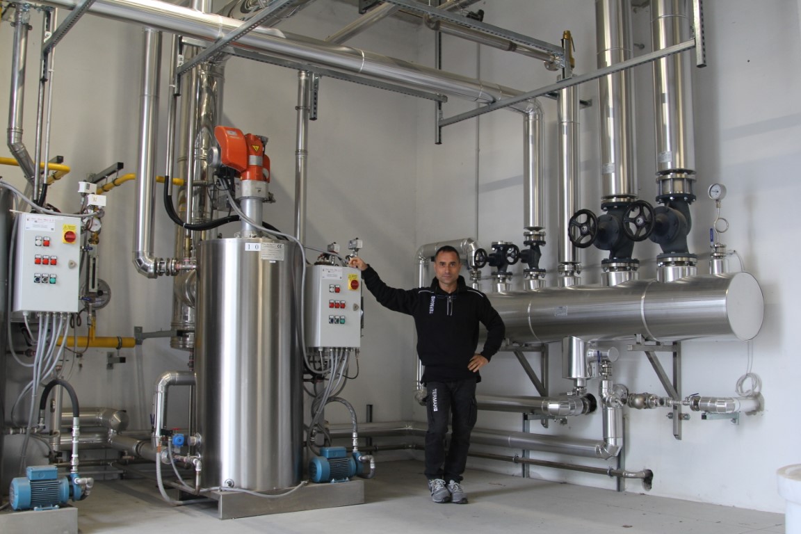 Tecnico Termak in piedi accanto a un impianto industriale in acciaio inossidabile composto da caldaie, pompe e tubazioni.
