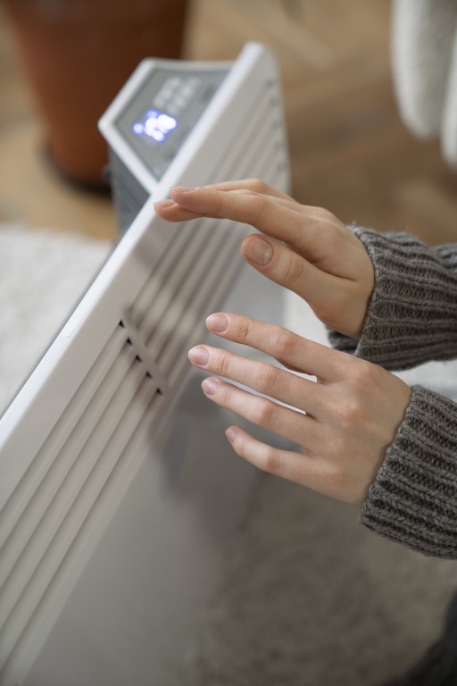 Primo piano di una persona che riscalda le mani davanti a un termosifone moderno.