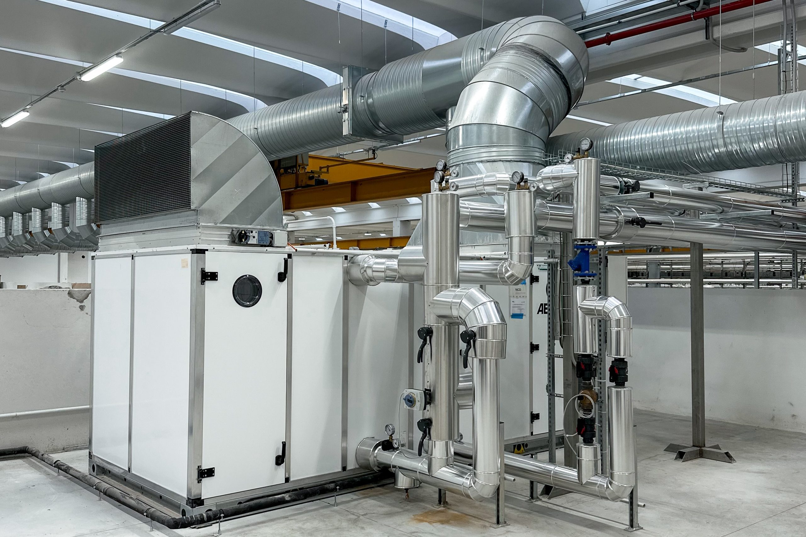 Sala impianti industriale con grande caldaia in acciaio, tubazioni isolate e quadro di controllo elettronico.